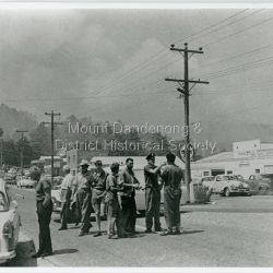 Taken during the 1962 bushfires. View of Mount Dandenong shops opposite the Hotel with garage to the right. 8 men in foreground with smoke clearly visible.