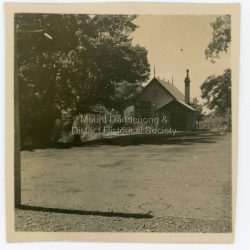 View of Mount Dandenong State School building taken in 1938. Shadow of netball post in the foreground.: On back of photograph: Mount Dandenong School 1938