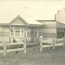 The Mount Dandenong Post Office & Store was originally built by Will Dower. The house and shop was built in 1912 and staffed by Ruby and Ada Dower. It became the Post Office in 1917 when Lil Badenhop sold her business following the death of her daughter Myrtle. The Post Office and Store closed in 1926 when the new premises opened on the Main Road.: Black & white photograph of Dower's house and shop built on the corner of Old Coach Road and Farndons Road in Mount Dandenong. A man, woman and two children are in the foreground. Donated as a jpeg digital image.