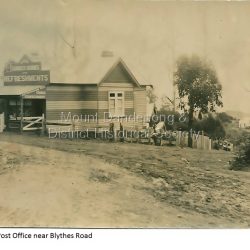 The Mount Dandenong Post Office & Store was originally built by Will Dower. The house and shop was built in 1912 and staffed by Ruby and Ada Dower. It became the Post Office in 1917 when Lil Badenhop sold her business following the death of her daughter Myrtle. The Post Office and Store closed in 1926 when the new premises opened on the Main Road.: Black and white photograph of Dower's house and shop built on the corner of Old Coach Road and Farndons Road in Mount Dandenong. A boy with a bicycle can be seen at the LHS edge of the photograph and the Mount Dandenong State School building directly behind the shop.