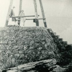 The Observatory on the high point of Mount Corrhanwarrabul was used to take trigonometrical readings from as early as 1850. The area became very popular with tourists as a place to walk and drive to. The SkyHigh restaurant is on the site of the Observatory.: Black and white photograph showing a stone base topped with a wooden structure. Two women are posed below the wooden structure.