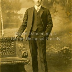 Studio photograph of Harry Booth. A young man wearing a dark, three piece suit, collar and tie. Included in the Dorey/Woolrich collection.: Black and white photograph of young Harry Booth taken in a formal studio setting. Harry Booth was the son of Jack Booth, who owned Lots 37 and 38 in the Village Settlement and had access to creek water for successful berry crops. Harry was a local market agent and travelled to Victoria Market carrying produce from local settlers.Harry carried a variety of produce by horse and cart, apparently a twenty-four hour round trip, until the business was sold in the early 1920's.: Harry Booth Eden Studios Post Card