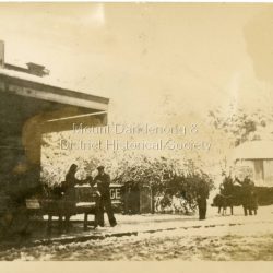 Small photograph showing people outside Gill's Store in the main street of Olinda with snow on the ground. Note Golf Course sign on the building in the background. c1950s.