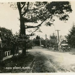 Number 10 in commercial series: Small photograph, number 10 in Olinda series, showing Main Street Olinda. View is looking NW from Olinda Monbulk Road towards Range Road. Left hand building is old Olinda Post Office. Ice truck is outside shops in distance and a delivery truck with tarp can be seen. c1930s