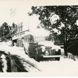 Small photograph showing a US Motors bus in Main Street Olinda under snow. US Motors depot in background. Late 1940s
