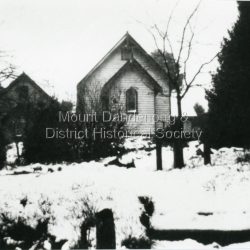View from Monash Avenue of St Matthew's Anglican Church with snow covering ground. The church was built in 1903, but this photograph is post 1935 as the Church Hall can be seen behind the trees on the left.