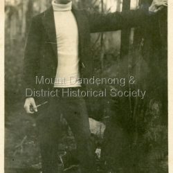 Photograph taken in 1914 of young man dressed in cap, rollneck jumper and jacket leaning on a tree. He is holding a pipe. The inscription on the back identifies him as 'Reg' with the surname 'Murry' added at a later date.: 5/9/14 This is awful, but as it was taken at Olinda, coming back from Outlook Rock, I send it. Reg (Murry)