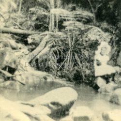 Young girl in a white pinafore and large, white hat sitting on a rock at the edge of Emerald Creek. Reverse of photograph has handwritten description by John Lundy-Clarke.: Emerald, Creek Emerald Creek with Jessie Wyles