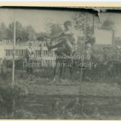 Scene from the Easter Monday Olinda Sports Carnival in 1909 with Alan Dodd clearing the high jump bar and Ernie Schneider standing to the left of the bar. The descriptive text on the reverse of this photograph was hand written by John Lundy-Clarke.: 1909 Alan Dodd clearing the bar. Ernie Schneider to the left of the bar.