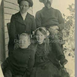 Mr Devine, Mrs Devine (nee Stewart) with children Vera and Stewart at their home 'Hillcrest' on Mernda Road (now Coonara road), Olinda 1911. The descriptive text on the reverse of this photograph was hand written by John Lundy-Clarke.: Devine, Mrs Devine (nee Stewart) Vera Stewart 1911 on verandah of Hillcrest Mernda Road now Coonara Road. Mrs Dodds collection. Copied by J.L.C. 1974.