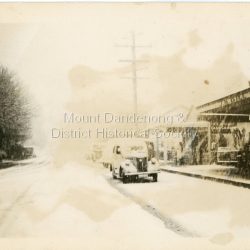 During heavy snowfall looking down Main Street Olinda towards Range Road. Old car parked outside J.H. Gill's store. c1950
