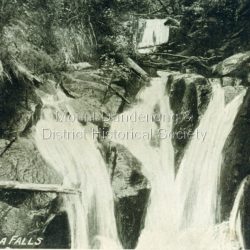 Copy of postcard captioned - Lower Olinda Falls that has a young man sitting on rocks at the upper LHS. This young man has been identified as Fred Dorey, brother of Iris Woolrich nee Dorey. The suggested date is after 1897 but before 1905. The Upper Olinda Falls can be seen in the background.: Printed on front: Lower Olinda Falls
