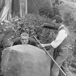 One man with a hammer and chisel makes to remove the others's ear