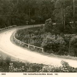 Sassafras - Olinda Road. Rocks in the foreground are on the property Nangana. The road is not yet metalled so it is c1920s.: Black and white Rose Series post card P. 1602 showing a sweeping bend on the Sassafas-Olinda Road.: On front: The Rose Series P. 1606. THE SASSAFRAS - OLINDA ROAD. VIC.